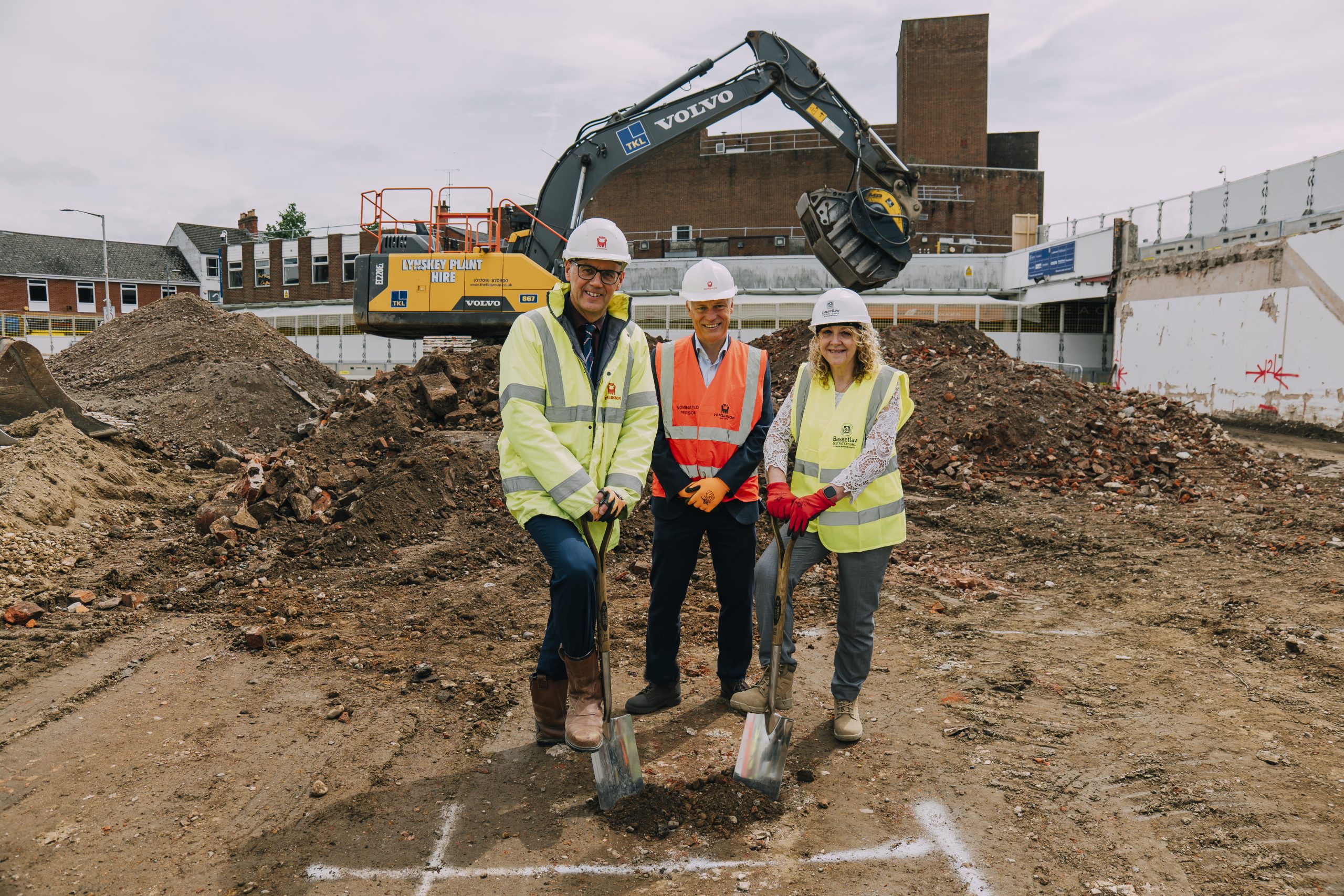 Three people stood on construction site, with two people breaking ground with a spade.
